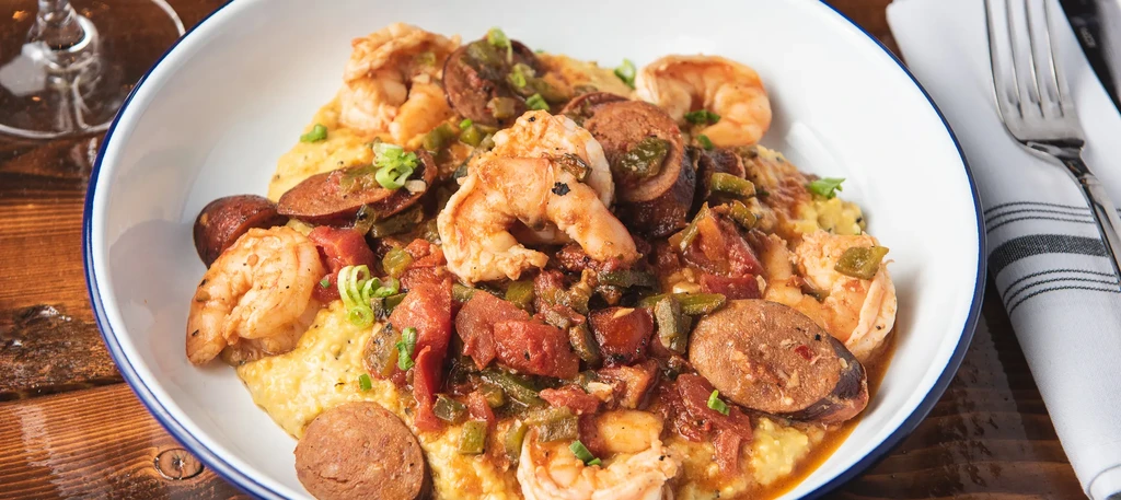 Close-up of shrimp and grits with sausage and vegetables in a white bowl.
