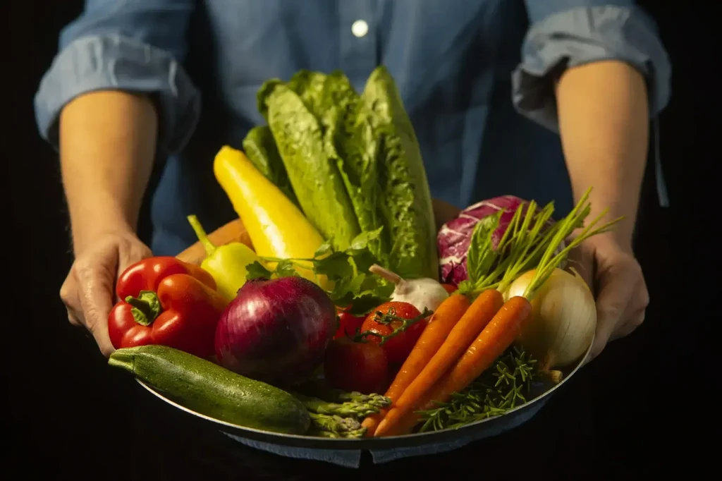 Person holds a platter overflowing with a vibrant assortment of fresh vegetables.
