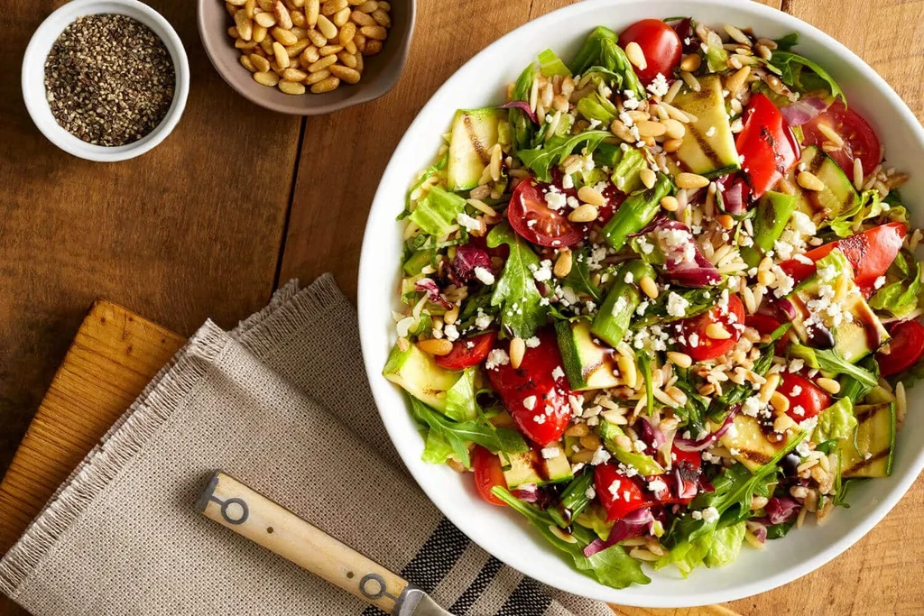 Vibrant salad with grilled zucchini, feta, pine nuts, and balsamic glaze.