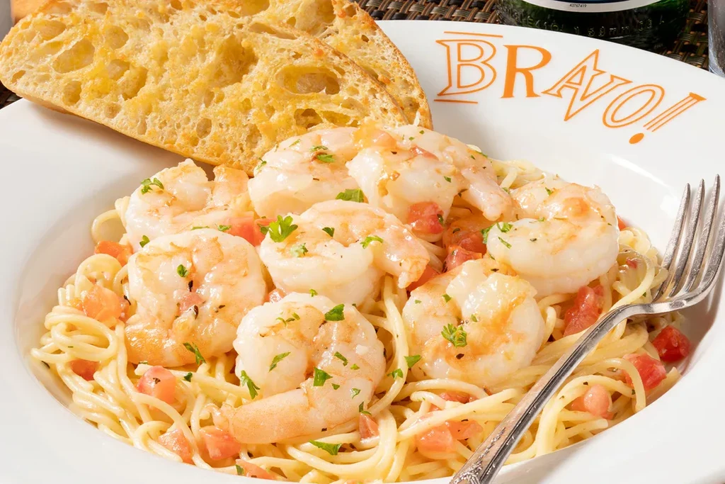 Appetizing bowl of shrimp pasta with tomatoes, parsley, and toasted bread.