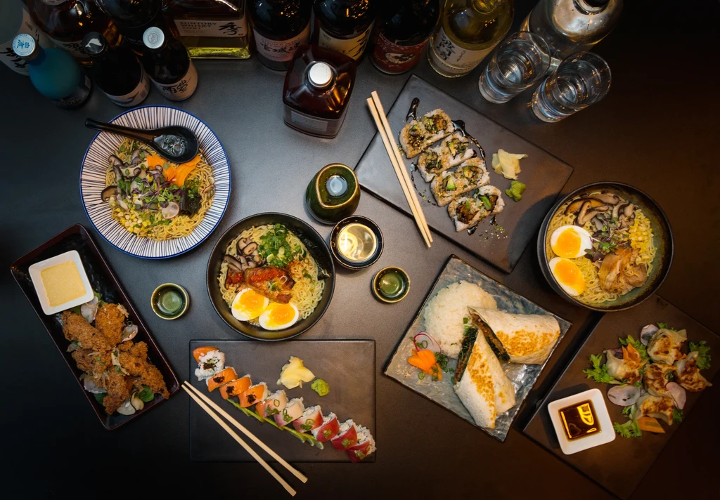 Flat lay of diverse Asian dishes, ramen, sushi, dumplings, and drinks.