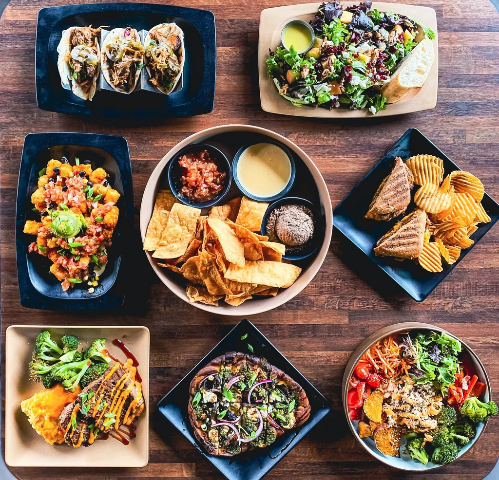 Overhead shot of eight diverse dishes on a dark wooden table.