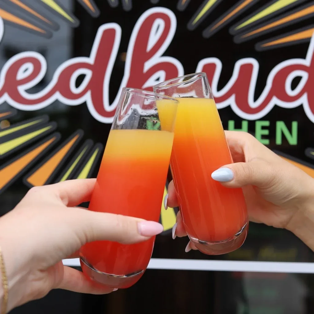 Hands clink orange and yellow layered drinks at Redbud Kitchen.