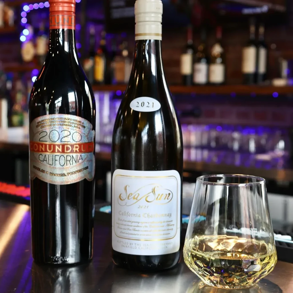 Conundrum red and Sea Sun white wine bottles, wine glass on bar.