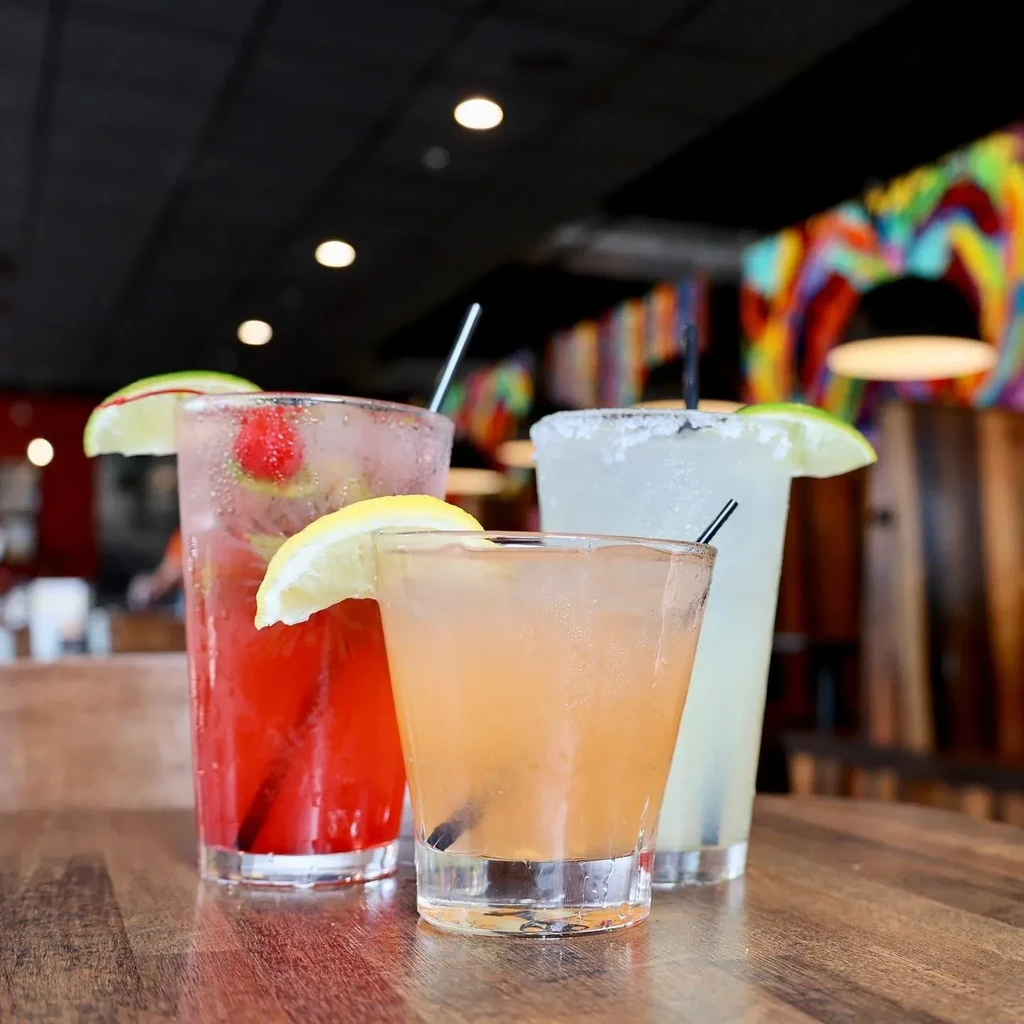 Three cold, garnished drinks (red, amber, light) on a dark table.