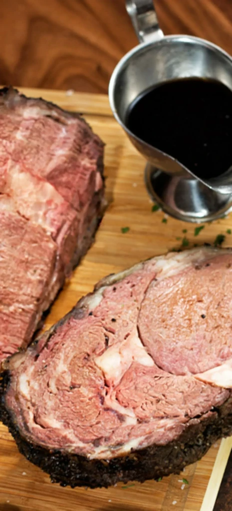 Two cuts of medium-rare roast beef on a wooden board with gravy.