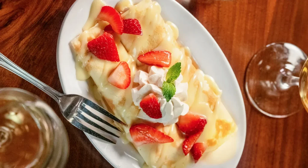 Dessert crepes with strawberry slices, whipped cream, and mint garnish.