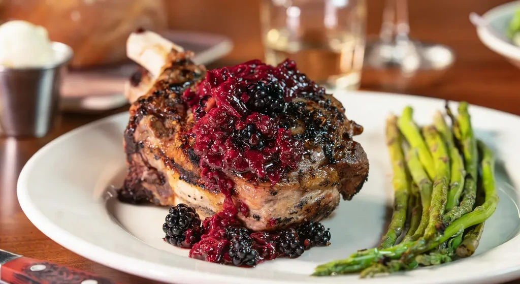 Bone-in grilled chop, blackberry compote, and asparagus on a white plate.