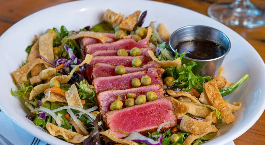 Seared tuna salad with mixed greens, vegetables, and sauce in a bowl.