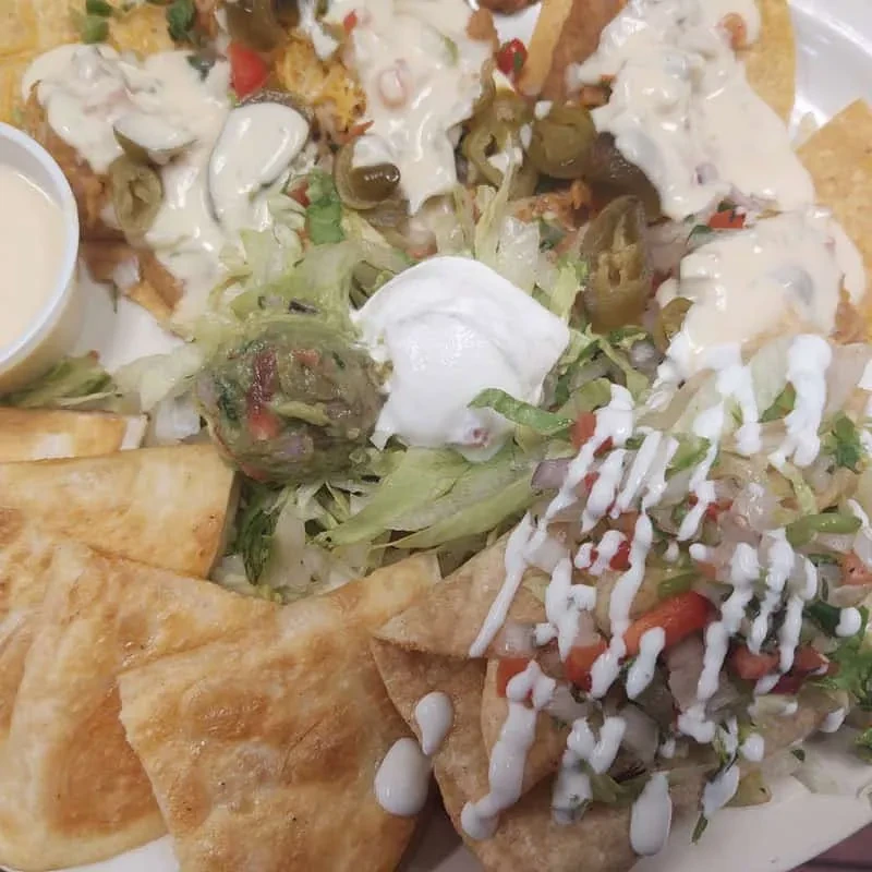 A large platter of heavily topped nachos, folded items, and Mexican dips.