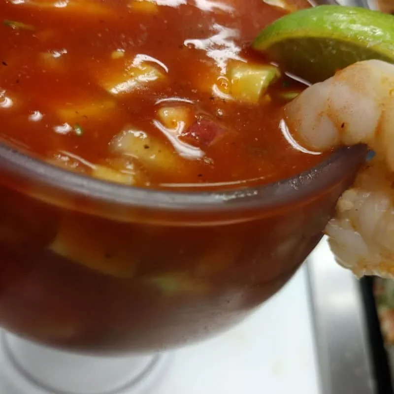 Close-up, soft-focus seafood cocktail with shrimp, lime, and diced ingredients.