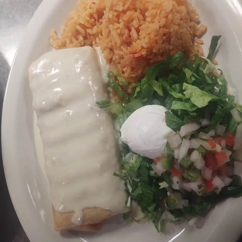 Mexican plate with creamy sauced burrito, orange rice, and side salad.