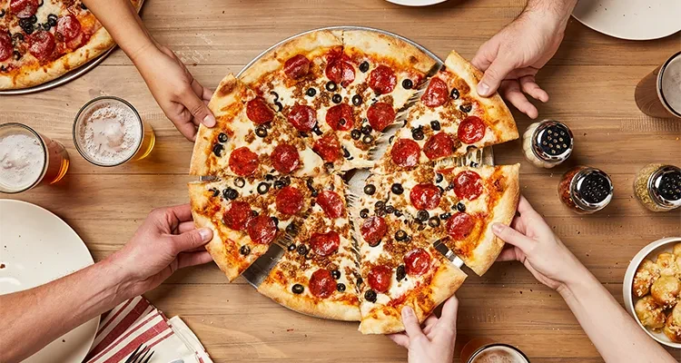 Overhead view: hands sharing a pepperoni, sausage, olive pizza with beer.