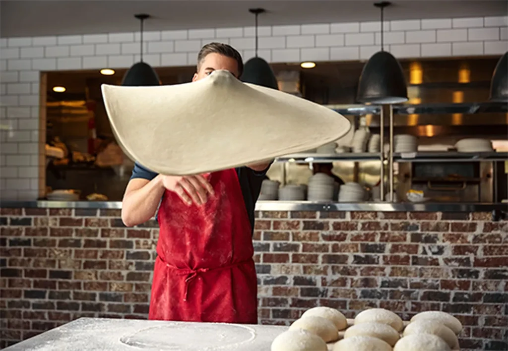 Chef in red apron tosses pizza dough high in a kitchen.
