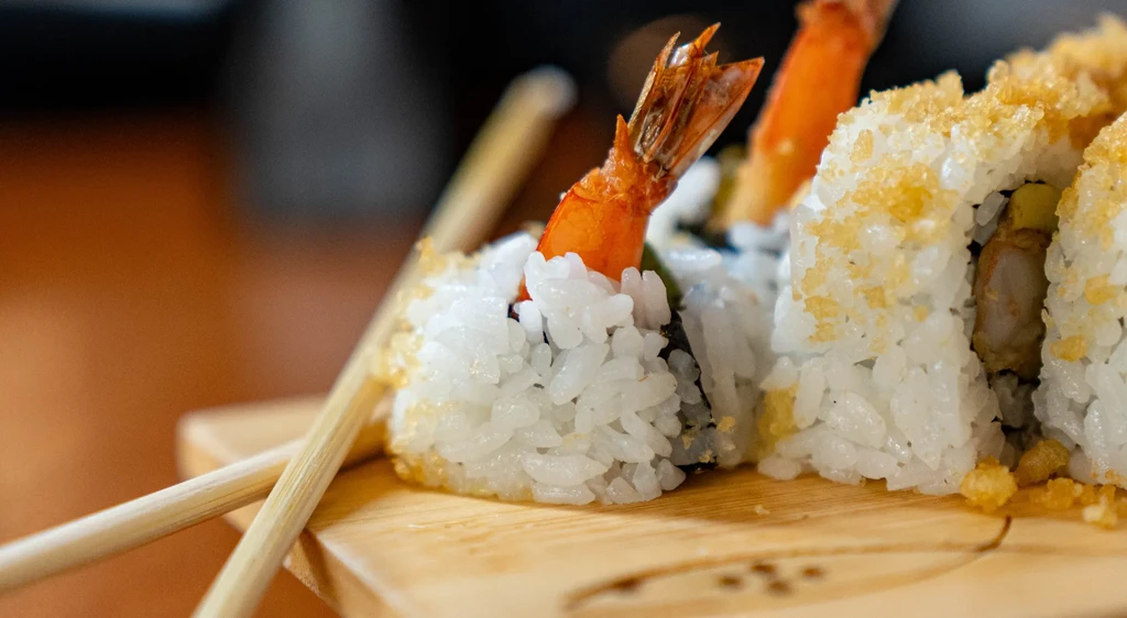 Shrimp tempura sushi rolls with chopsticks on a wooden serving board.