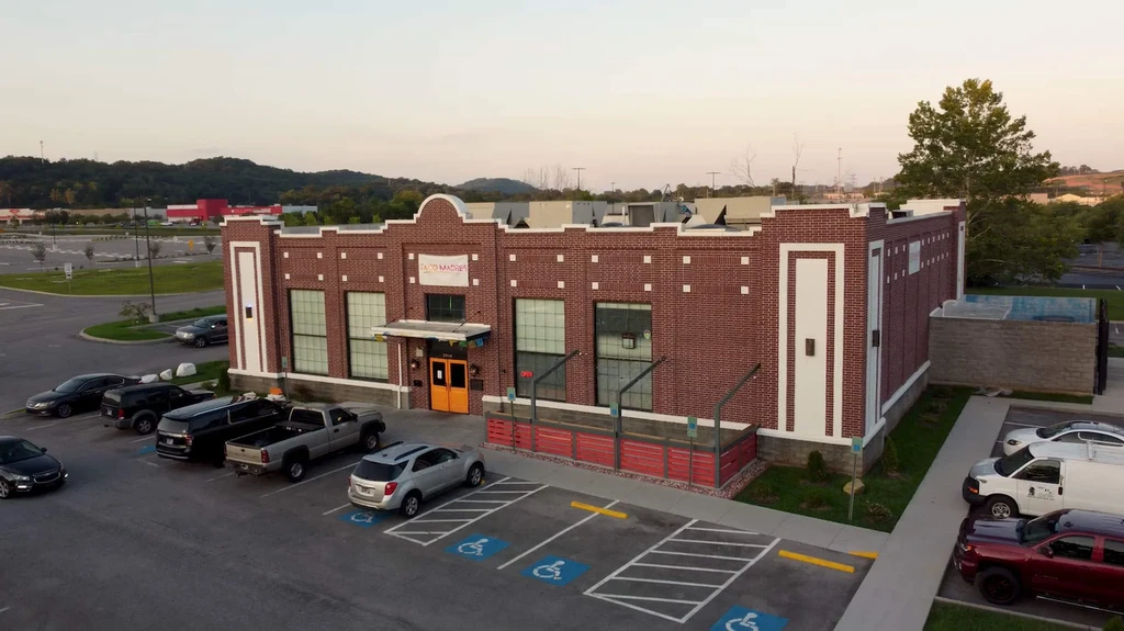 Aerial view of red brick Taco Madre restaurant, patio, and parking lot.