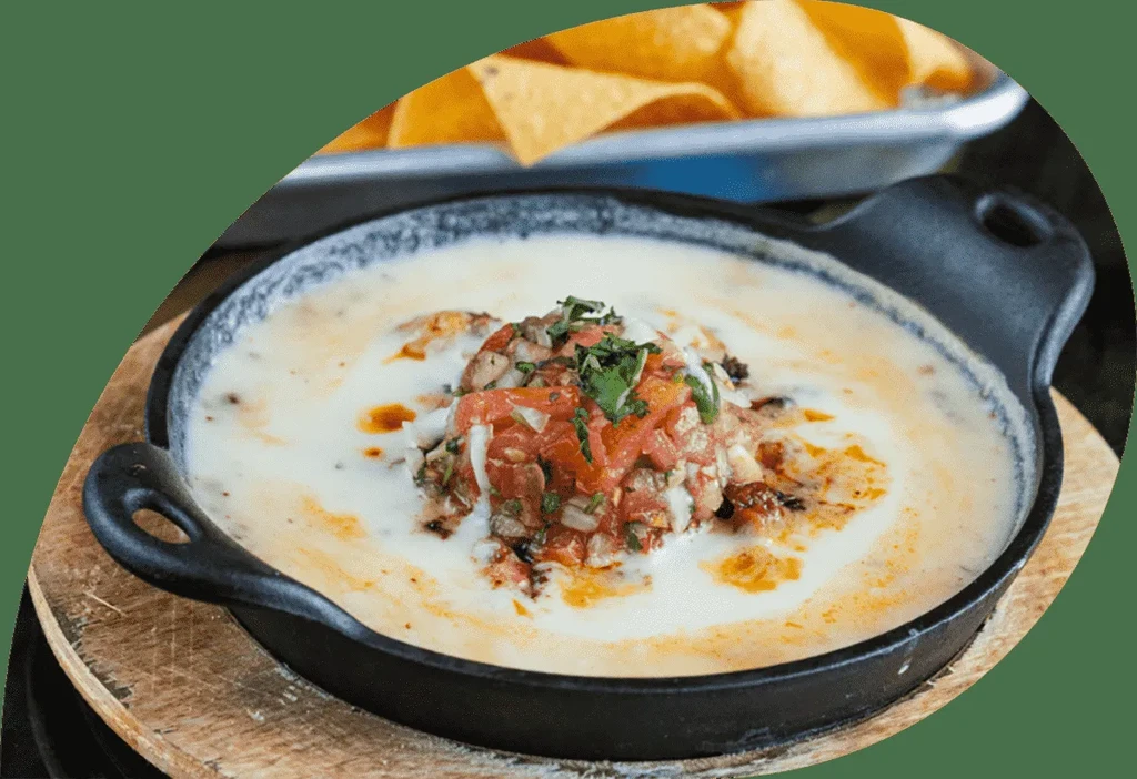 Bubbling cheese dip with pico de gallo in a black skillet.