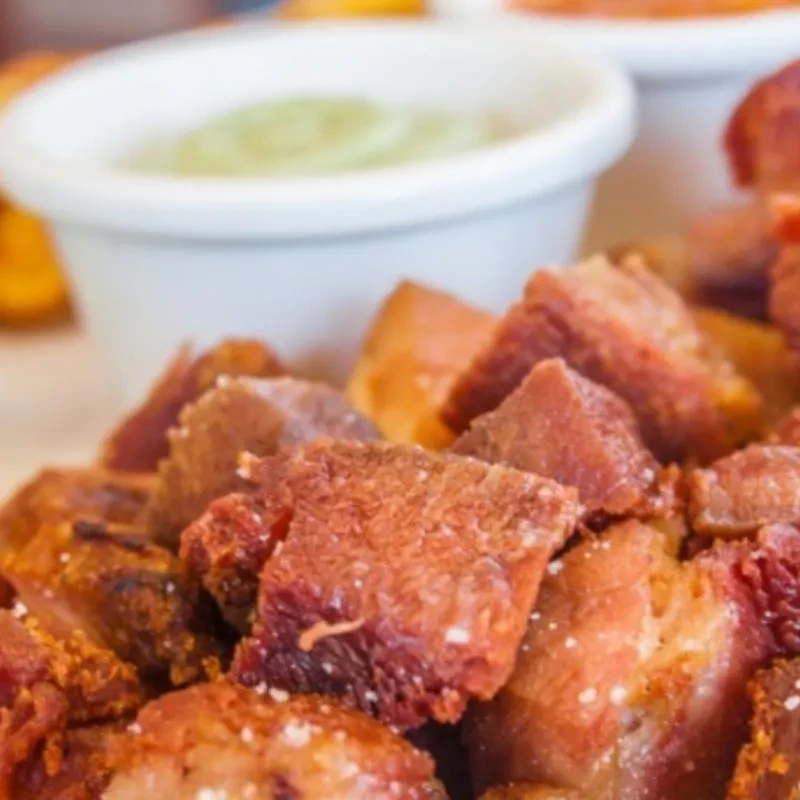 Close-up of heavily salted, crispy pork belly cubes and dipping sauces.