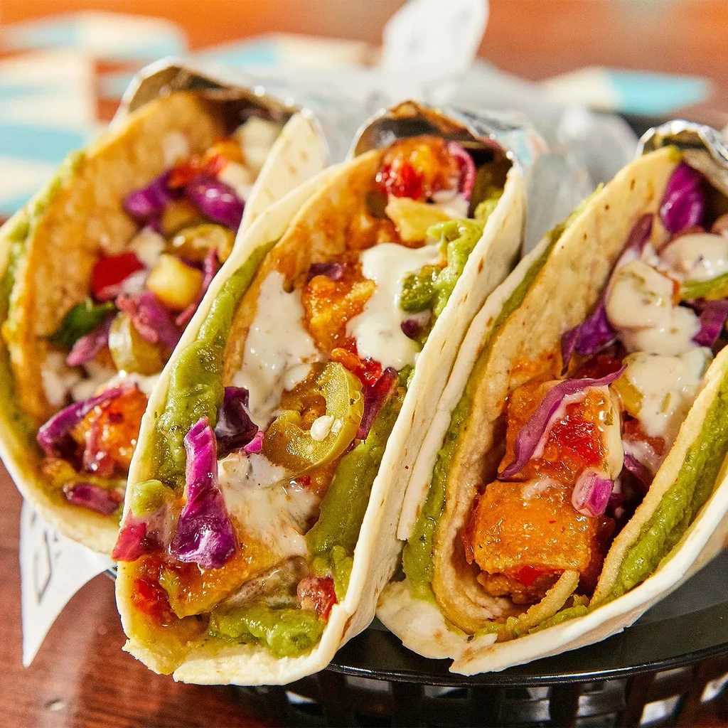 Three tacos with fried fish, colorful toppings, in a serving basket.