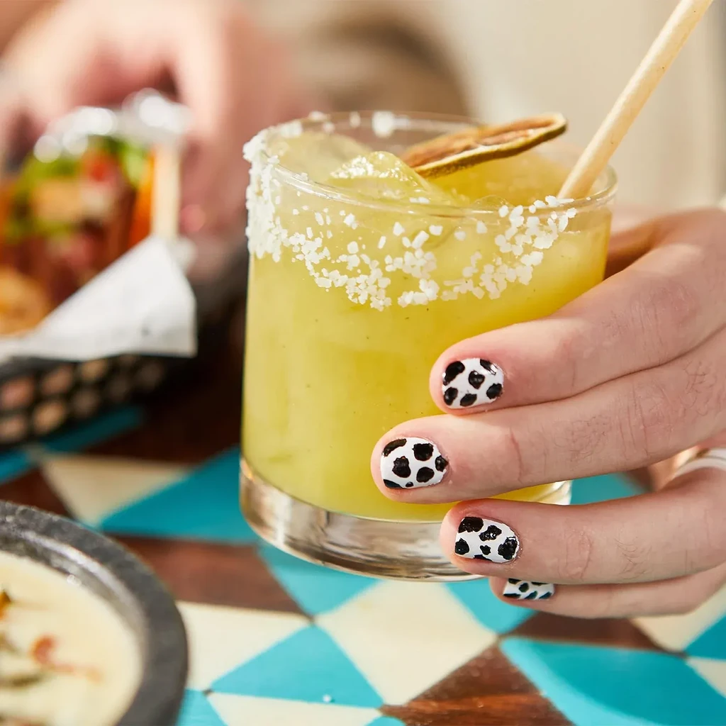 Cow-print nails hold a green drink with a salted rim.