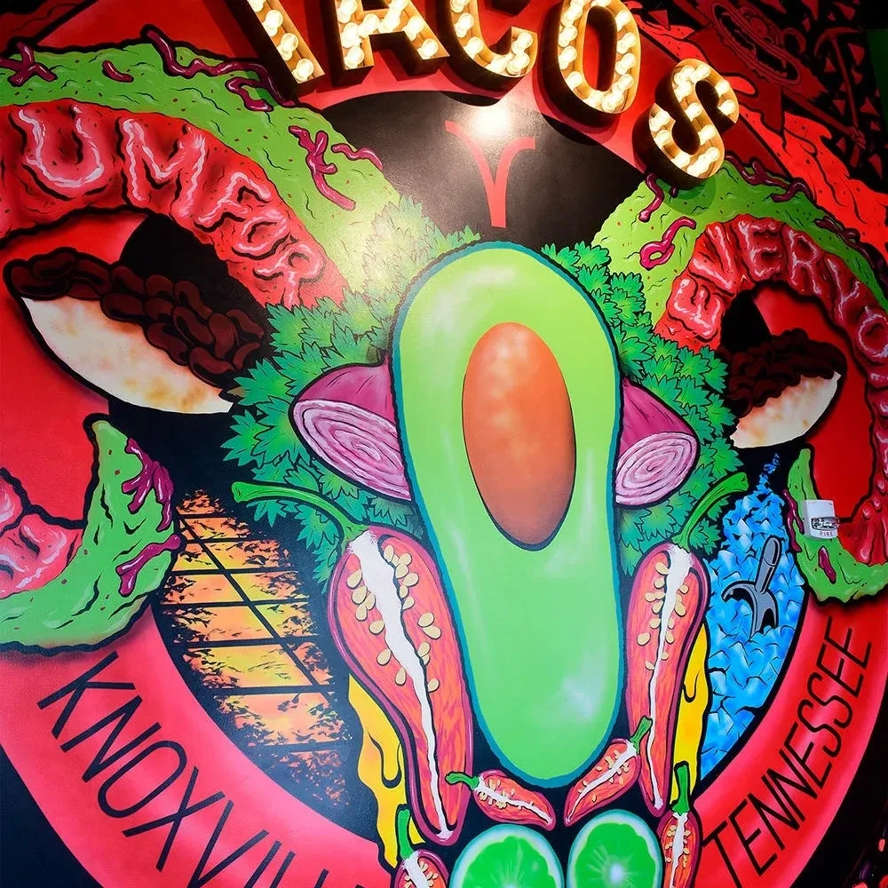 Colorful mural of taco ingredients, 'TACOS' marquee sign, Knoxville, Tennessee.
