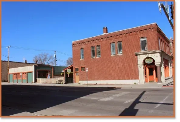 Sunny street: ornate red brick "The Local" and green-sided building.