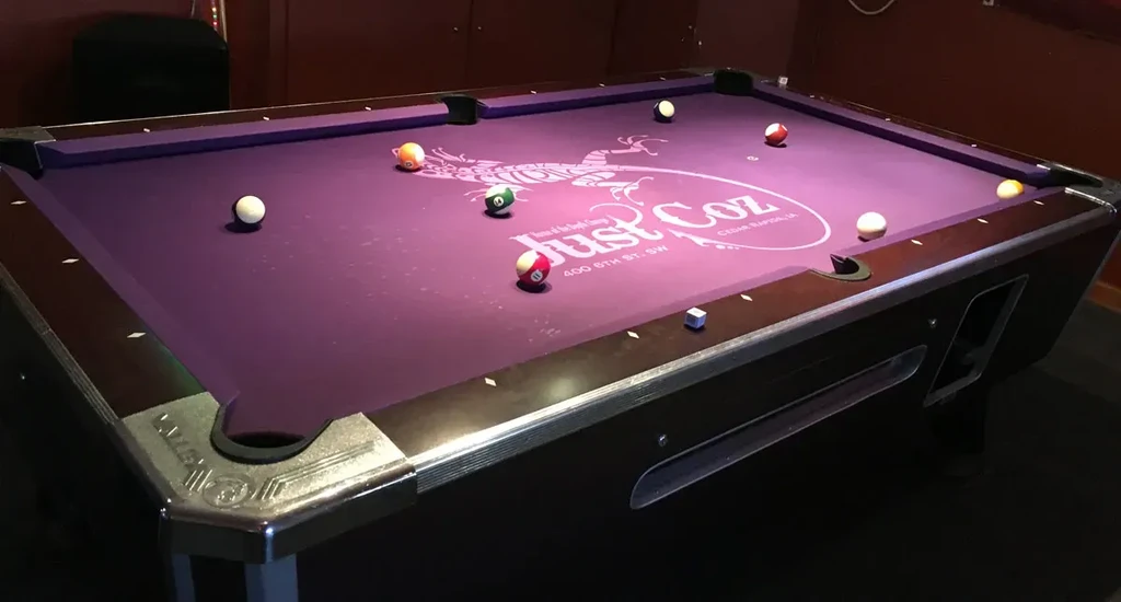 Purple felt pool table with balls and "Just Coz" logo.