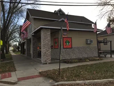 Brown restaurant exterior with American flags, outdoor seating, and autumn leaves.