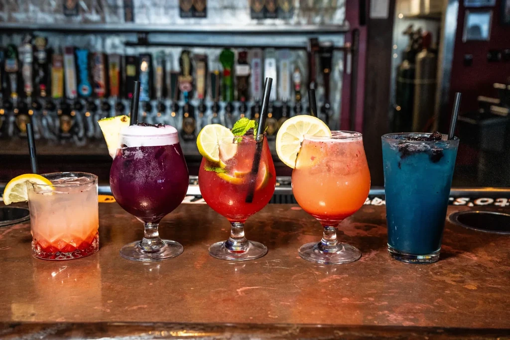 Five colorful cocktails in a row on a bar with beer taps.