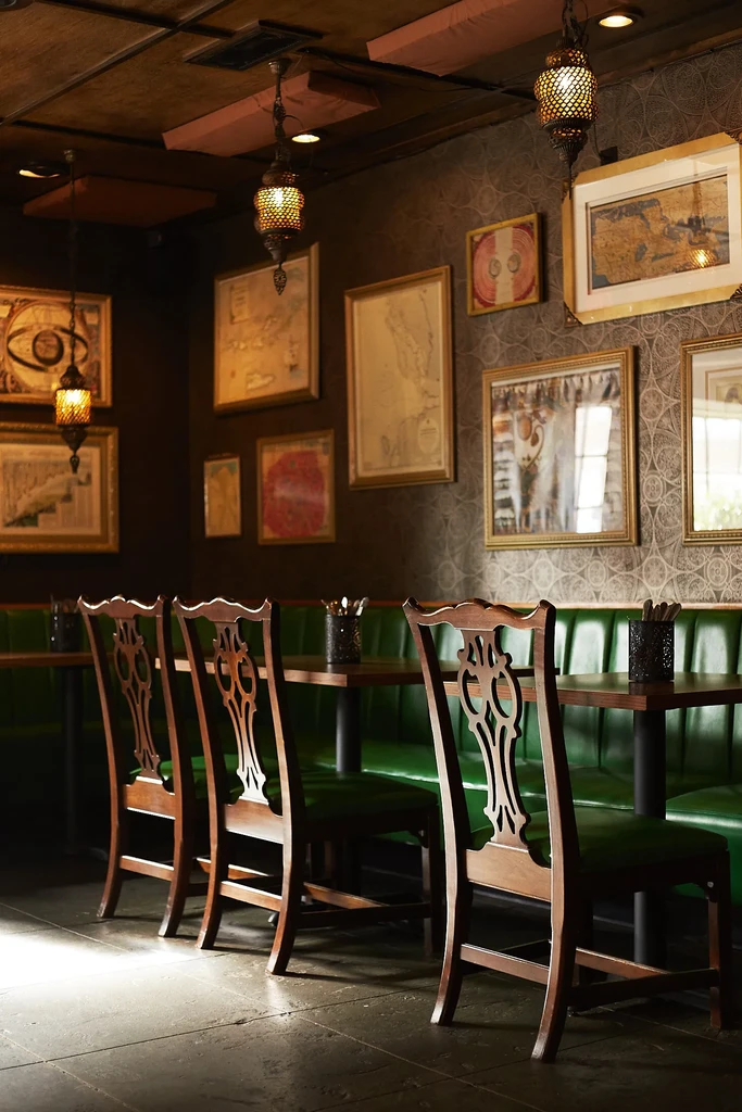 Cozy restaurant interior with emerald green booth, wooden chairs, and framed art.