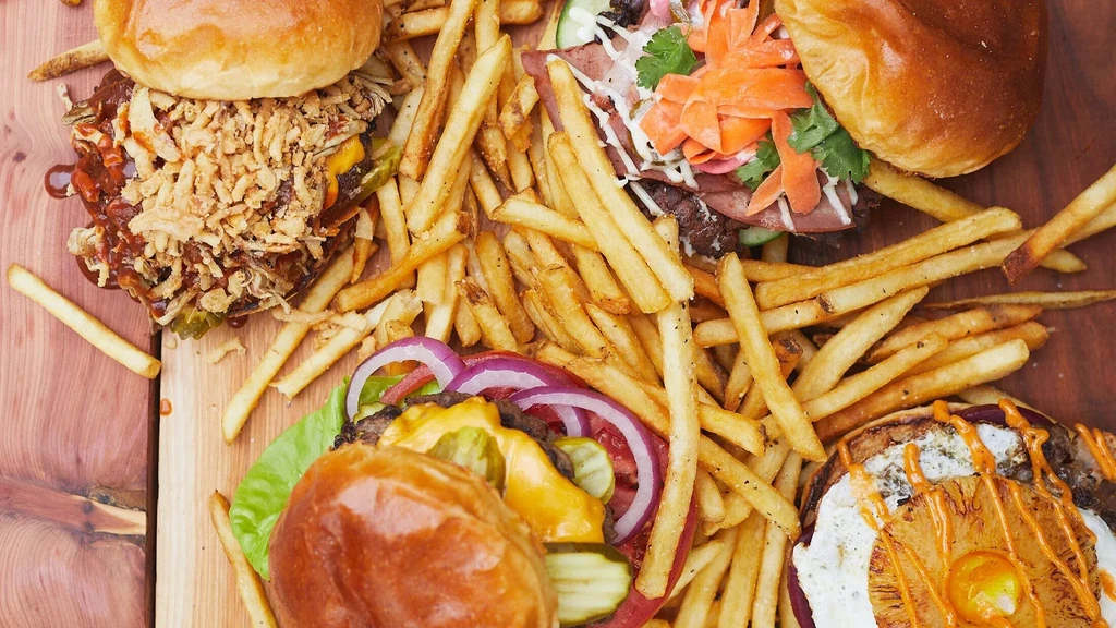 Overhead view: four gourmet burgers and golden french fries on a wooden surface.
