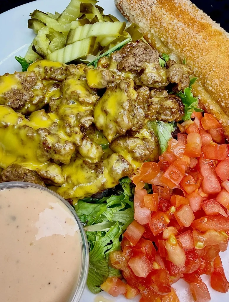 Deconstructed cheeseburger bowl with meat, cheese, lettuce, pickles, tomatoes, and bread.