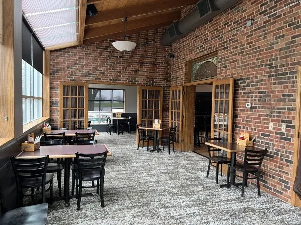 Empty restaurant dining room with brick walls, wooden beams, and square tables.