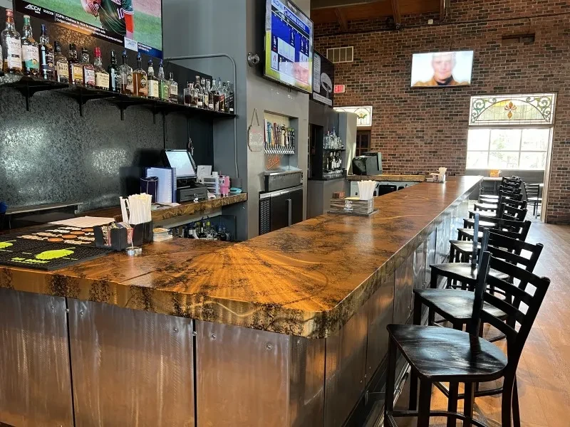 Empty modern sports bar with metallic bar, TVs, and liquor bottles.