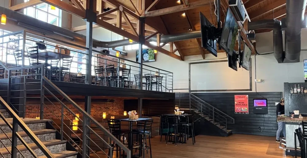 Spacious, multi-level industrial-rustic restaurant interior with TVs.