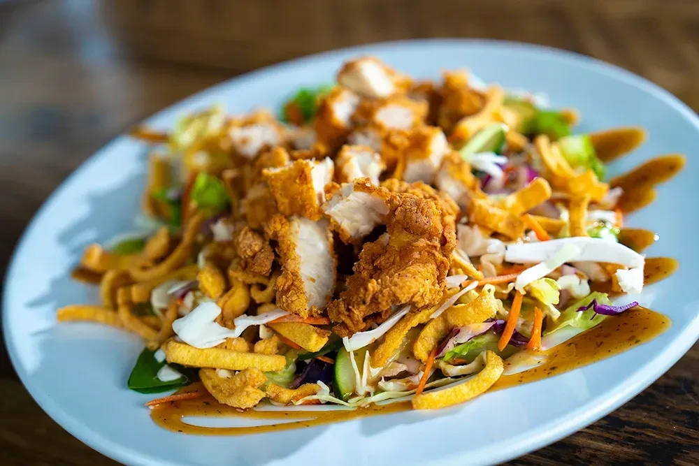 Fried chicken salad on an oval plate with greens and brown dressing.