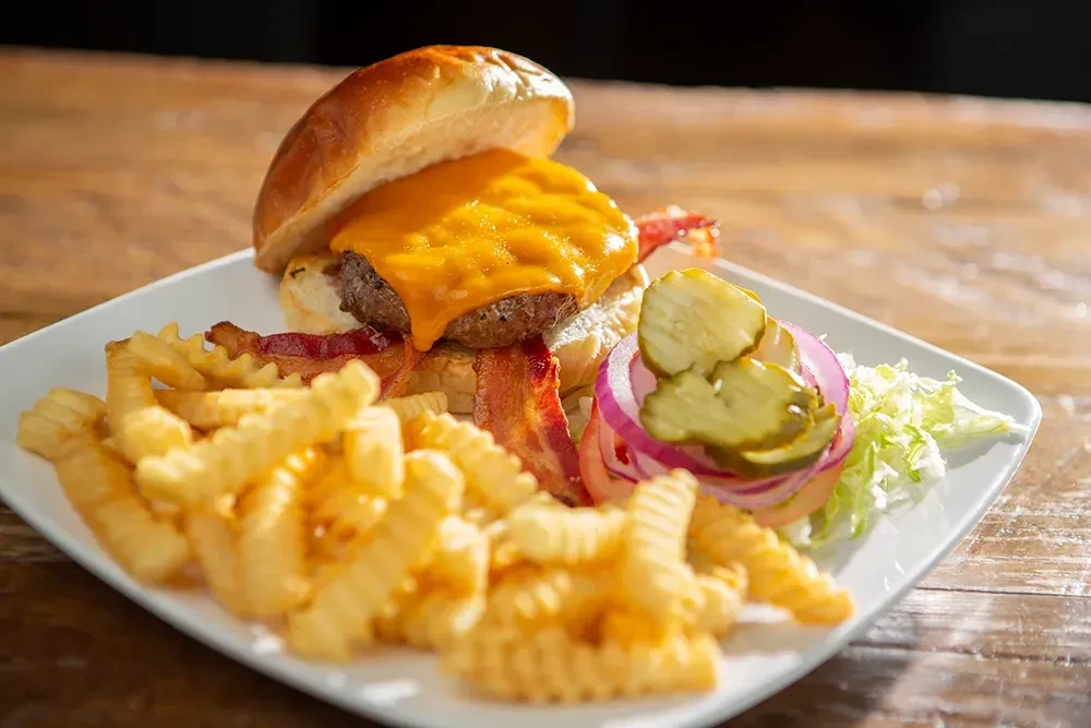 Cheeseburger, bacon, crinkle-cut fries, and fresh toppings on a plate.