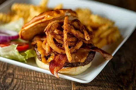 Close-up: Gourmet burger with bacon, cheese, fried onions, salad, and fries.