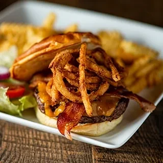 A gourmet burger with bacon, cheese, fried onions, salad, and fries.