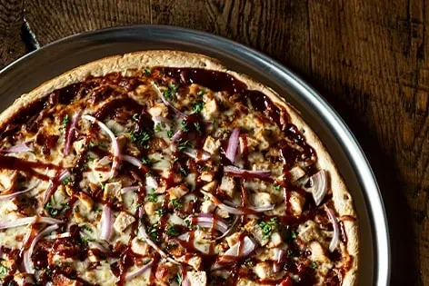 Overhead BBQ chicken pizza with red onion, herbs on wood.