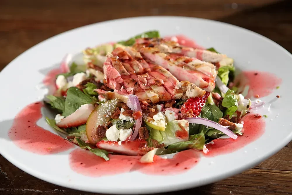 High-angle close-up of gourmet chicken salad with strawberries and dressing.