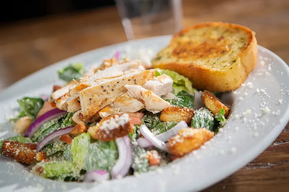 Close-up of grilled chicken Caesar salad with garlic bread.