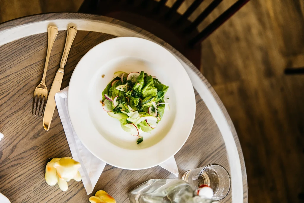 Plate of fresh green salad, cutlery, and glass on wooden table.