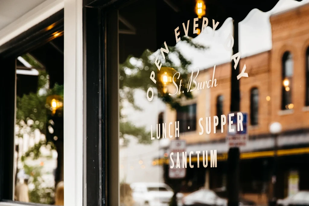 St. Burch restaurant window showing 'OPEN EVERY DAY' text and street reflection.