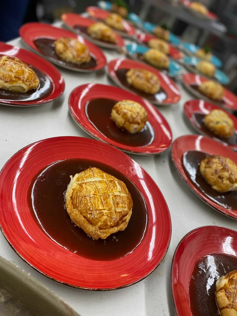 Rows of red plates with pastry-wrapped savory dishes and brown sauce.