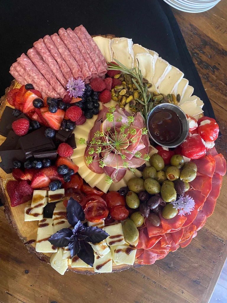 Circular wooden charcuterie board with meats, cheeses, fruits, and nuts.