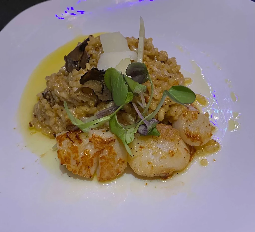 Seared scallops and truffle risotto with shaved cheese and microgreens.