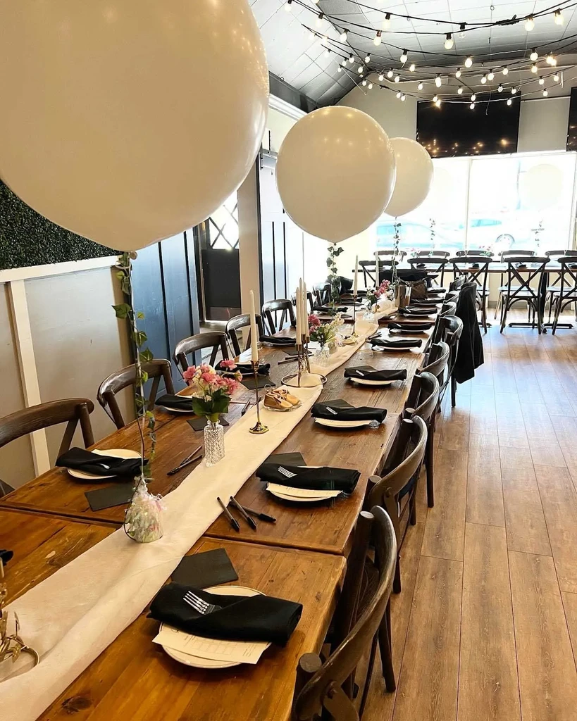 Event space with long rustic table decorated with flowers, balloons, and lights.