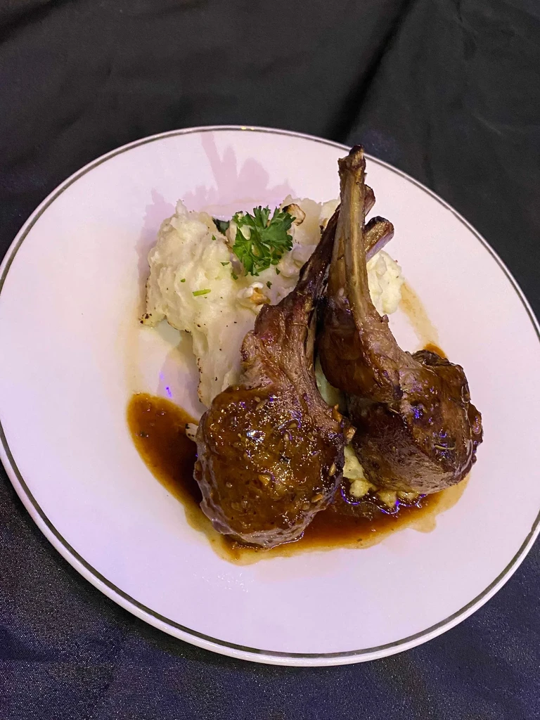 Two glazed frenched lamb chops with mashed potatoes and parsley.