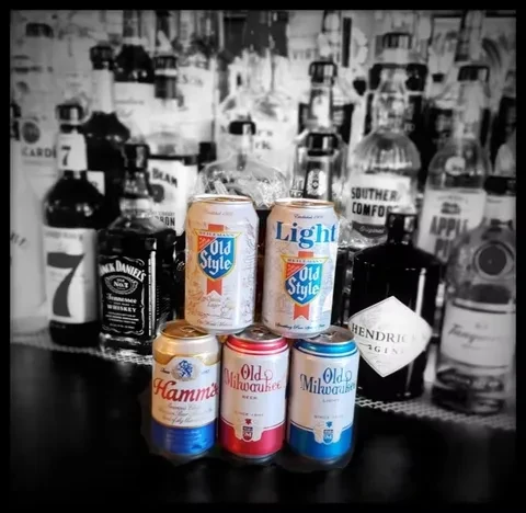 Colorful beer cans stacked against blurred, monochrome liquor bottles.